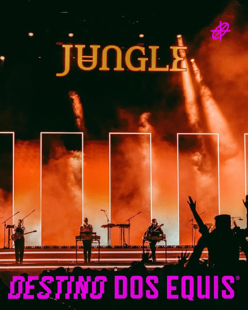 Fotografía de concierto en vivo con la banda Jungle en el escenario bajo luces naranjas, con el logo de Destino Dos Equis en la parte inferior.
