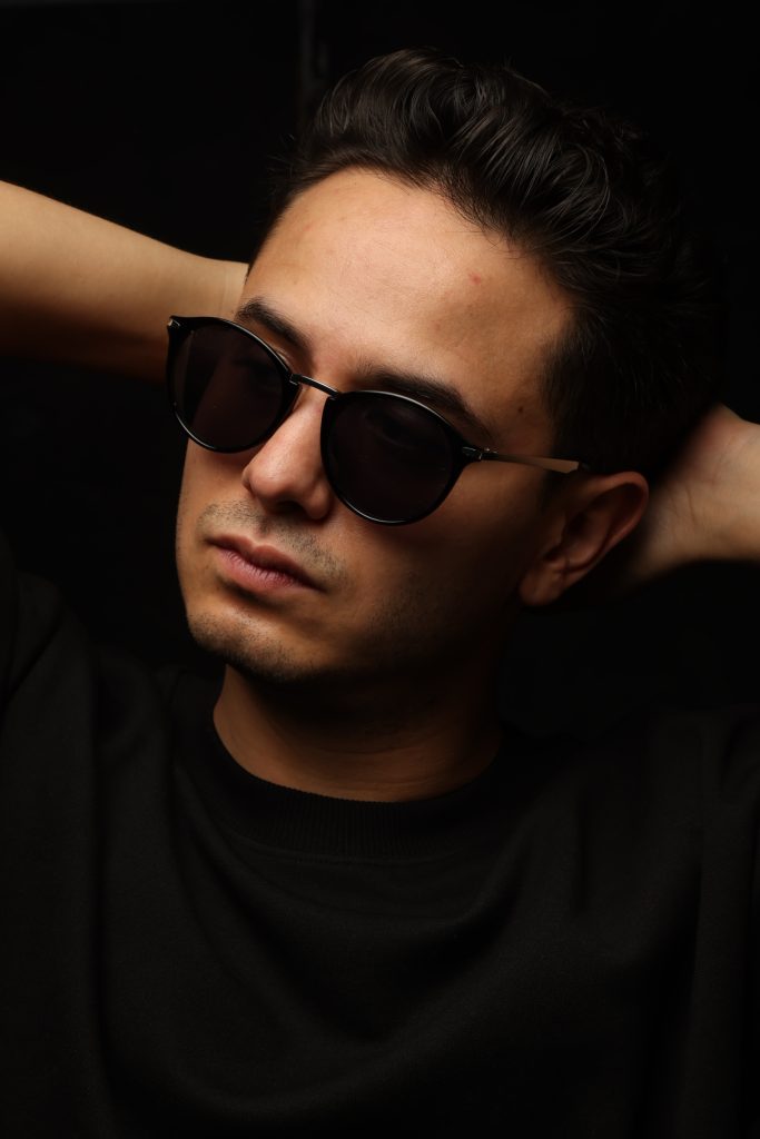 Primer plano de BZARS usando lentes de sol, con expresión seria y fondo negro, resaltando su estética minimalista.