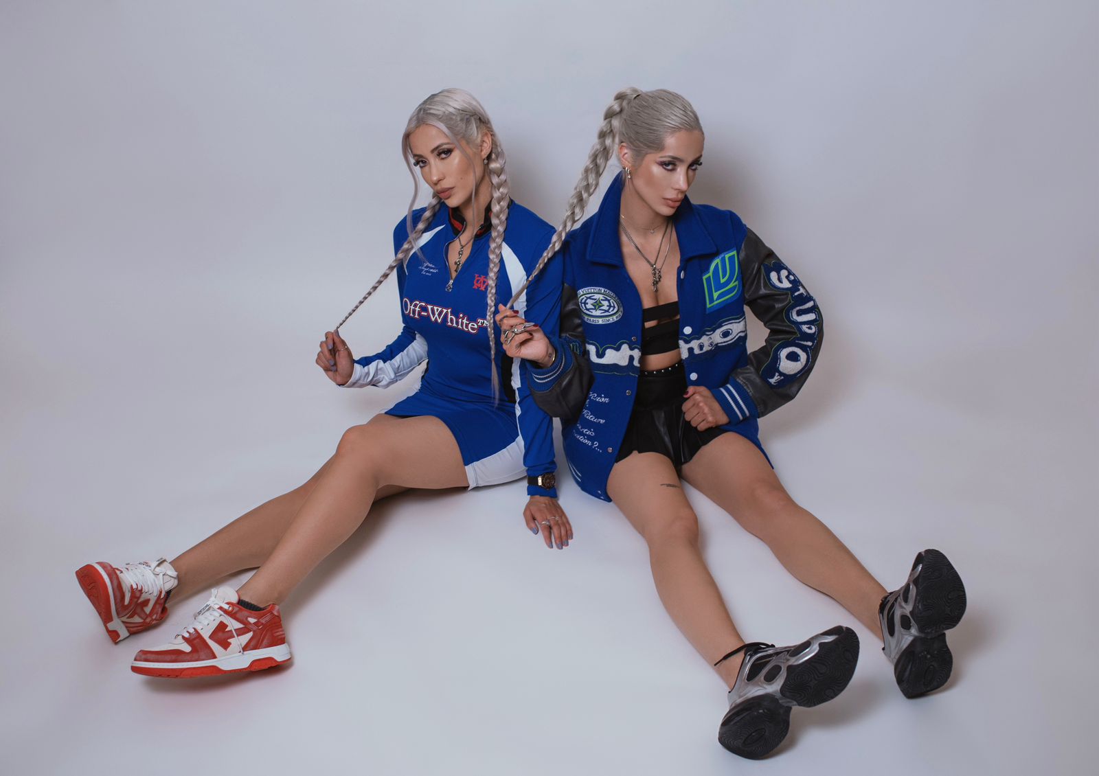 Le Twins en sesión fotográfica con outfits deportivos en tonos azules, posando sentadas sobre fondo neutro.