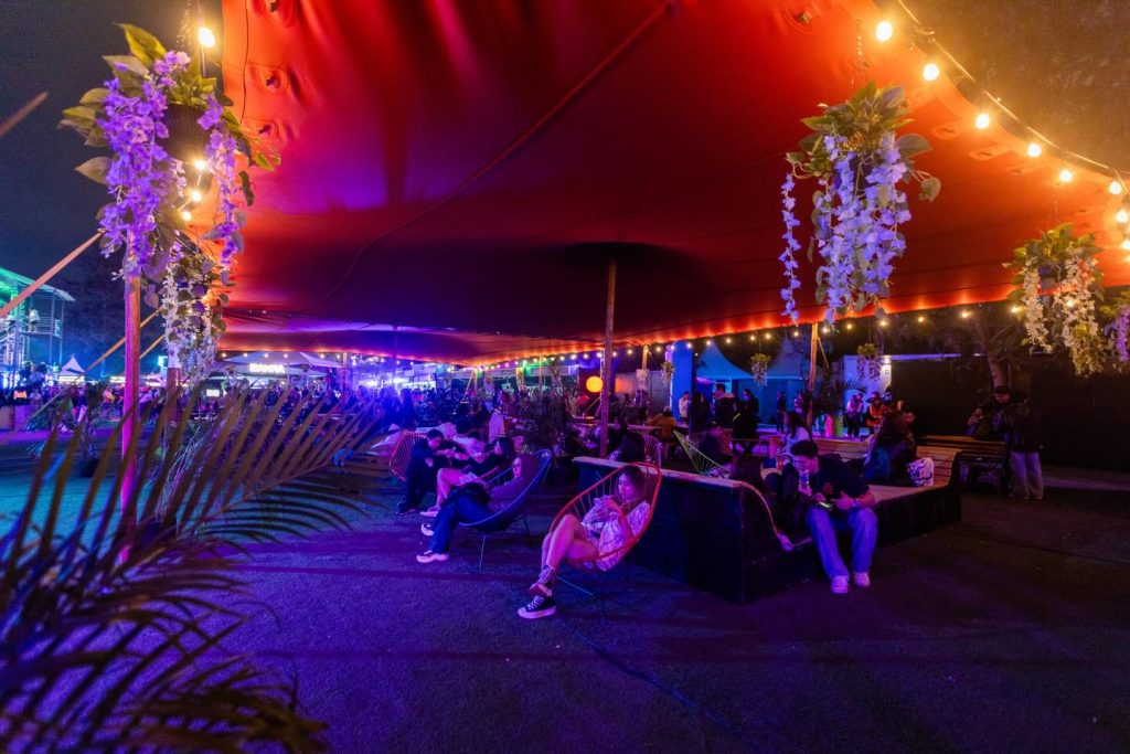 Zona de descanso del Área PLUS en EDC México durante la noche, con carpa iluminada, mobiliario tipo lounge y asistentes sentados recuperando energía dentro del festival.