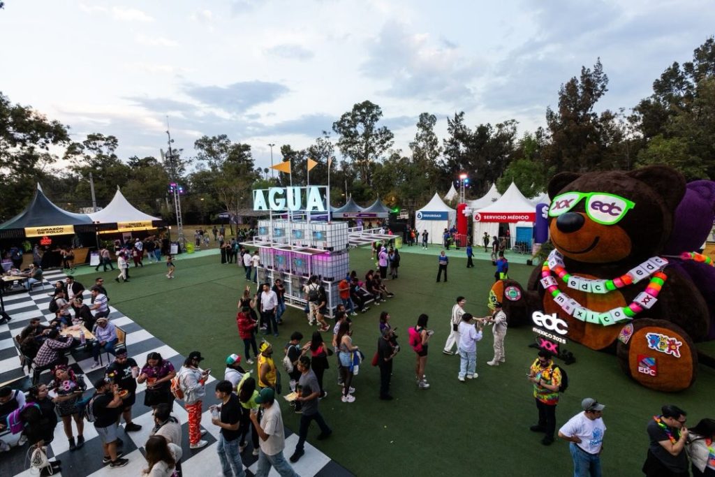 Vista general del Área PLUS en EDC México con asistentes caminando, módulos de servicios, zonas abiertas y elementos decorativos visibles desde una toma elevada.