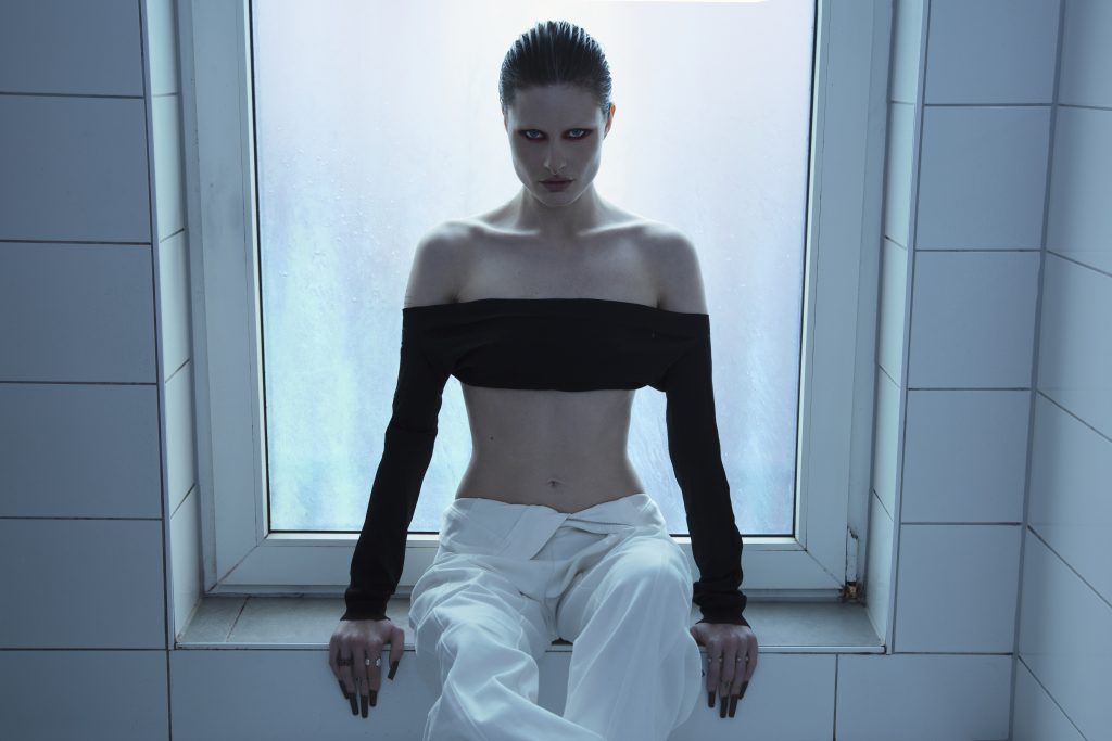 SPFDJ sentada frente a ventana con iluminación fría, referente del hard techno europeo que llega a México.