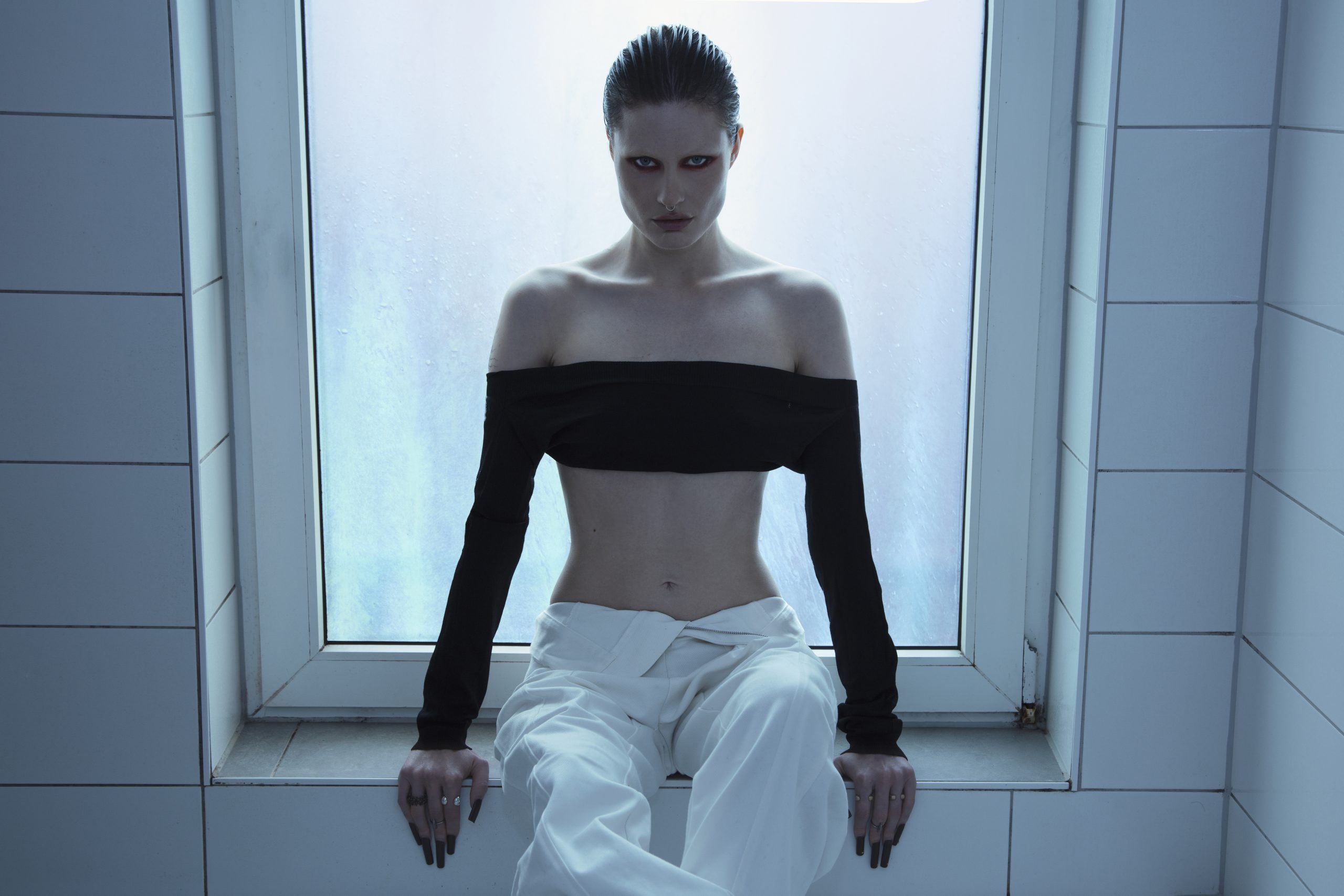 SPFDJ sentada frente a ventana con iluminación fría, referente del hard techno europeo que llega a México.