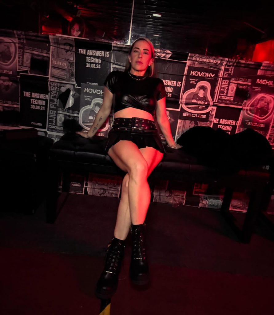 Shanti Clasing, productora de hard techno mexicana, en fotografía de prensa con iluminación roja en ambiente de club underground.