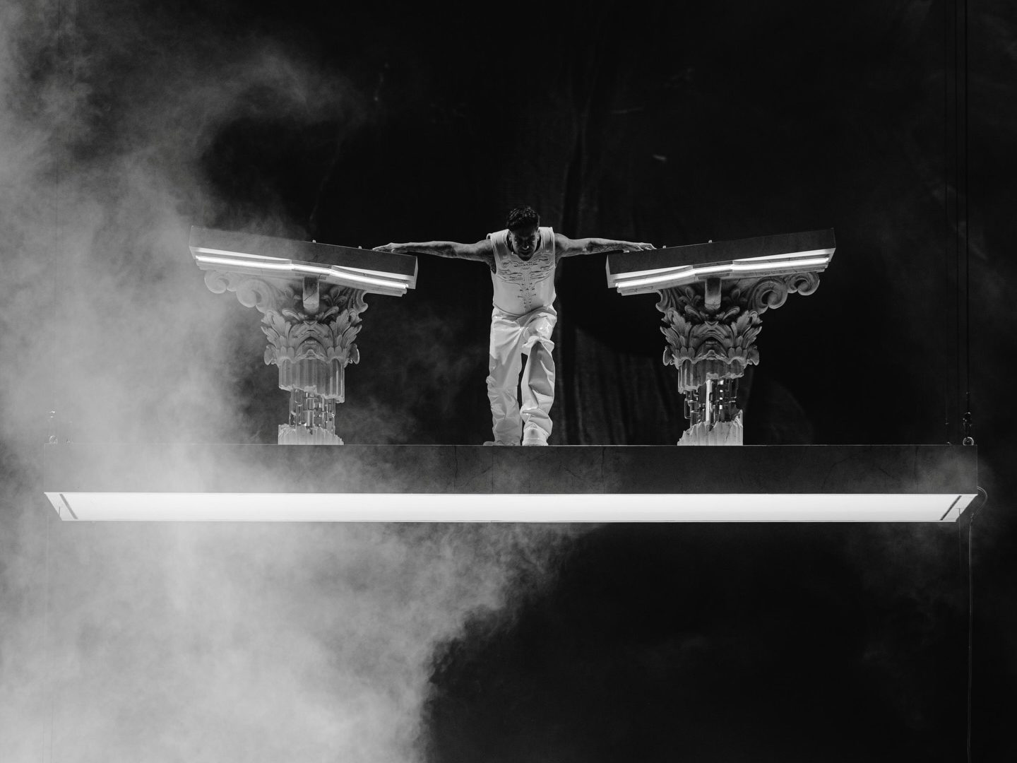Momento del show ÆDEN de Anyma sobre una plataforma suspendida flanqueada por columnas corintias iluminadas, con humo escénico envolviendo el escenario